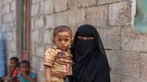 A mother holds her child in her arms. Together, they pose for a photo in Yemen.