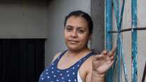 A woman stands against a wall and poses for a photo.