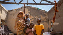 A mother stands with her three children in the ruins of a destroyed building in Sudan.