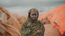 A woman poses solemnly for a photo outside of a makeshift shelter in Somalia.