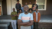 The family stand in front of their house, smiling.