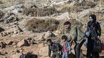 A family walks through an arid landscape with their belongings.