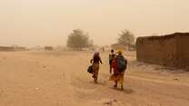 IRC staff members walk through a sandstorm outside of a town in Mali.