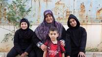 A mother sits outside with her three children. The family has been displaced from their home in Lebanon.