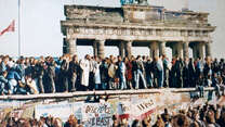 Menschen stehen jubelnd auf der Berliner Mauer vor dem Brandenburger Tor während des Mauerfalls 1989.