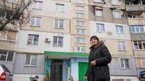 Kateryna stands in front of her apartment in Ukraine, which shows shelling damage