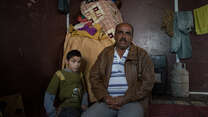 Abu Raed sits with his son Bashar, who is paralyzed, in their family's caravan at the Zaatari refugee camp in Jordan.