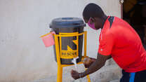 Man in red top using an IRC water station to wash his hand