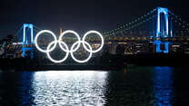 Night view of illumiated Monument of Olympic Rings, set on a barge in Tokyo with a bridge behind it 