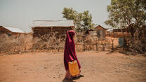 In Ethiopia, a girl walks along a dusty village lane carrying a jerry can to collect water for her family.