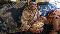 An Afghan woman displaced by drought sits holding her baby inside a tent.