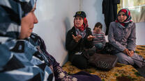 An IRC staff member talks with a Syrian refugee family seated on cushions in their shelter in Zaatari refugee camp in Jordan.