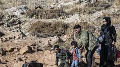 A family walks through an arid landscape with their belongings.