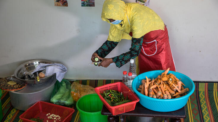 Sajida cuts cucumber into slices, surrounded by bowls of different vegetables.