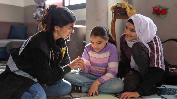 An IRC staff member, Ameera, and her sister sit together at an IRC Safe Healing and Learning Space. Together they complete a learning activity.