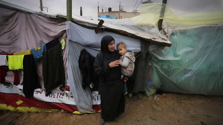 A woman holds a young child outside a makeshift shelter in Gaza.