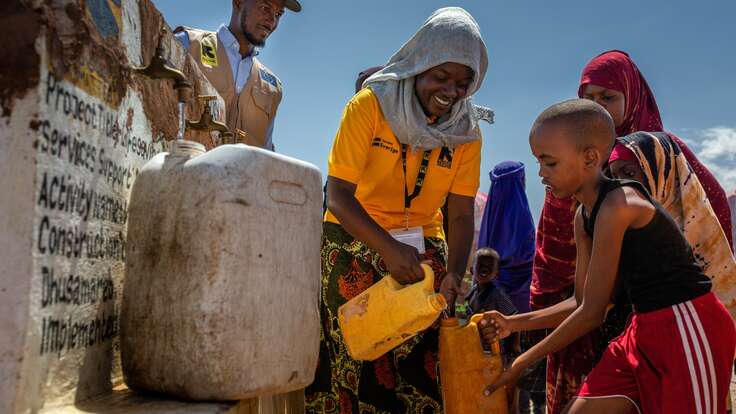 An IRC workers helps a young person fill up their water container at a water collection point in Somalia.