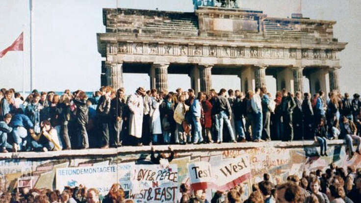 Menschen stehen jubelnd auf der Berliner Mauer vor dem Brandenburger Tor während des Mauerfalls 1989.