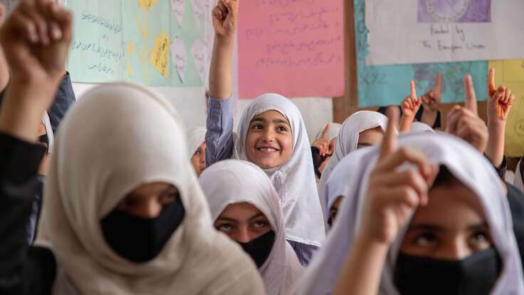 A student raises her hand and smiles while she attends a class in Afghanistan.