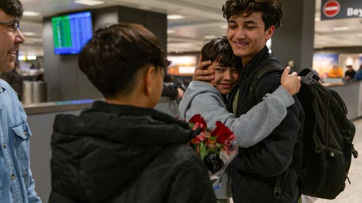 A family is reunited at an airport in the U.S. Two brothers embrace in a tight hug.