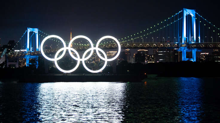 Night view of illumiated Monument of Olympic Rings, set on a barge in Tokyo with a bridge behind it 