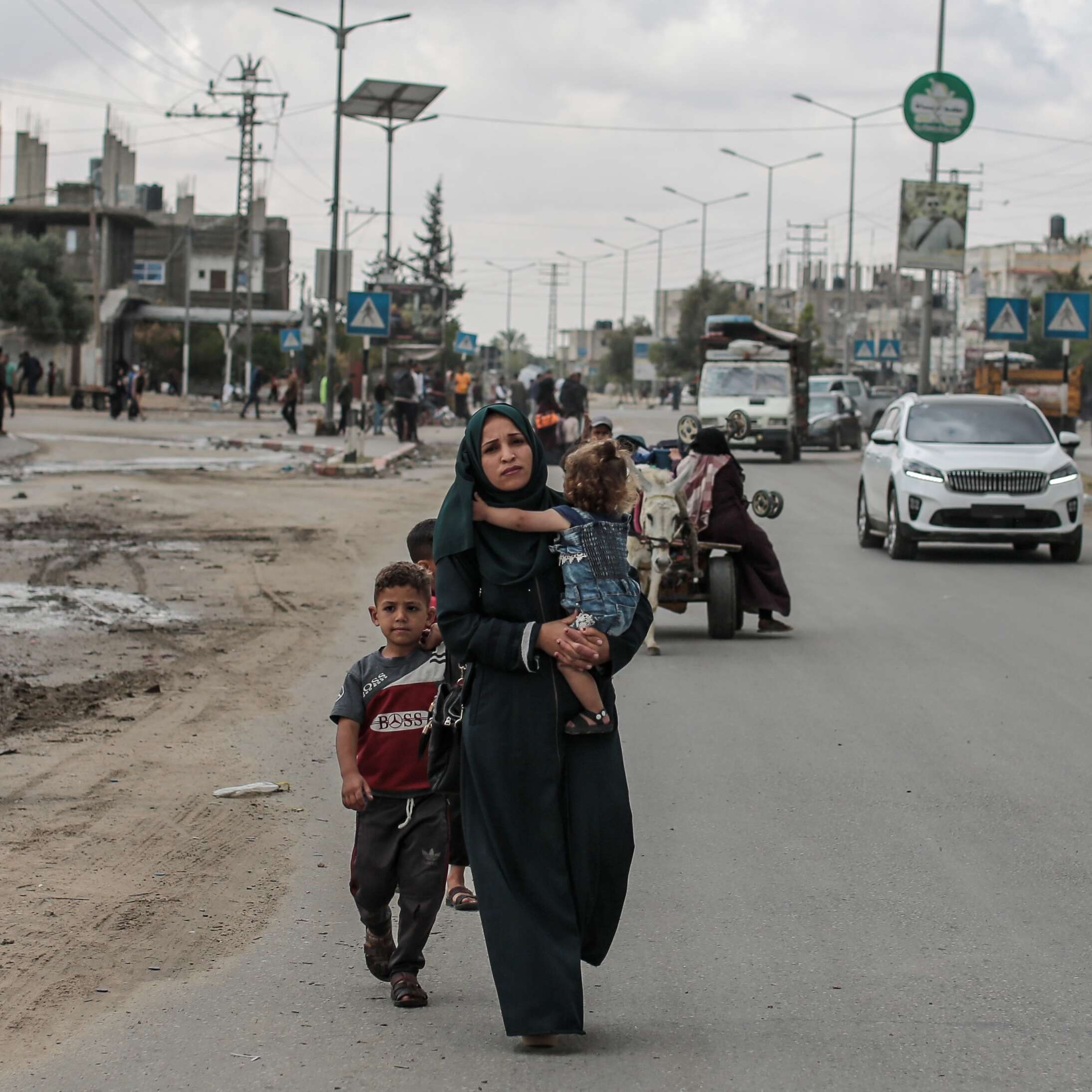 A mother walks on the road, carrying her daughter with her two boys by their side as they migrate from Rafah towards Khan Younis in Gaza.